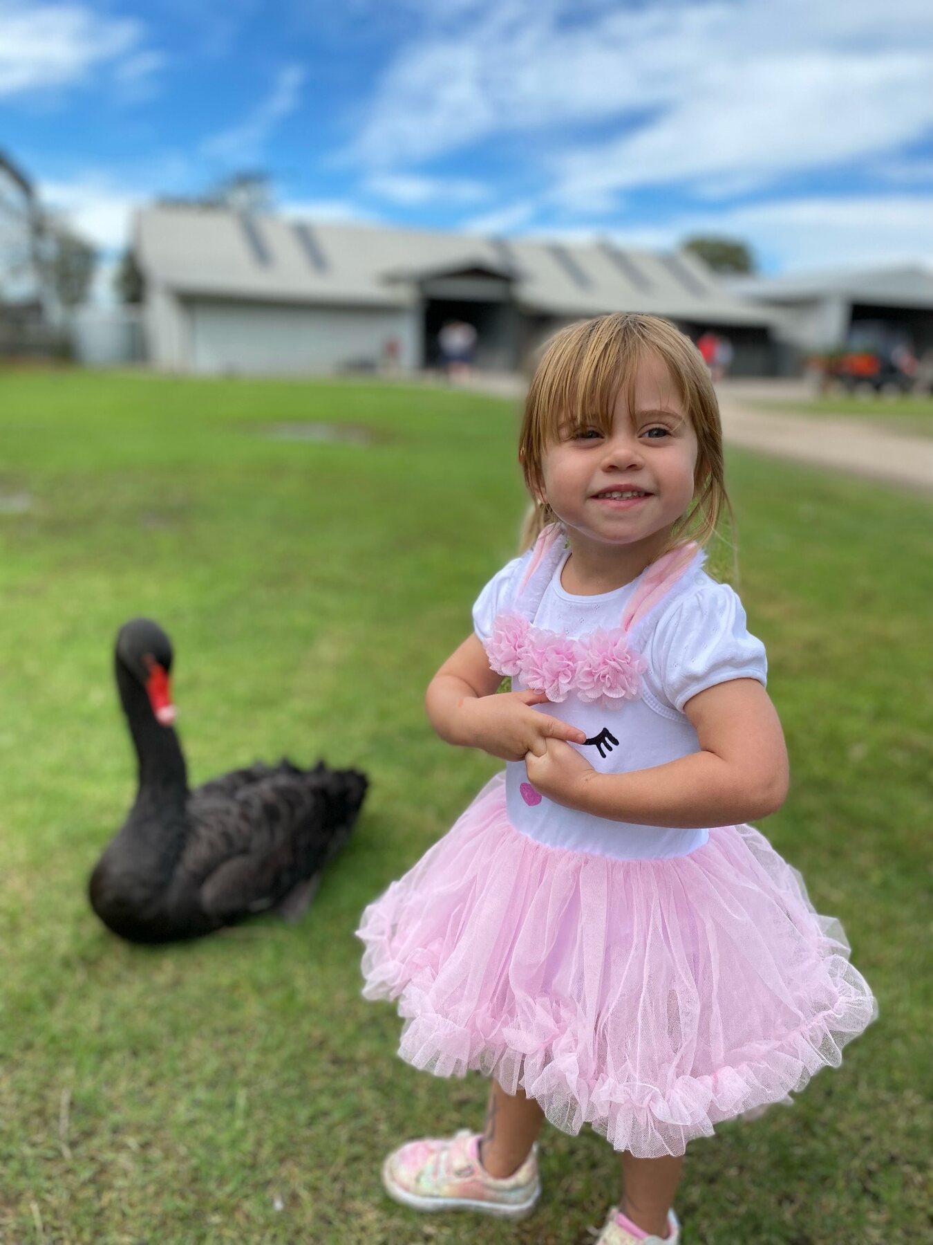 Flo smiling in her pink dress beside a black swan